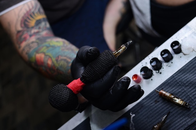 Il tatuatore crea un'immagine sul corpo di un uomo. primo piano di macchinette e mani per tatuaggi