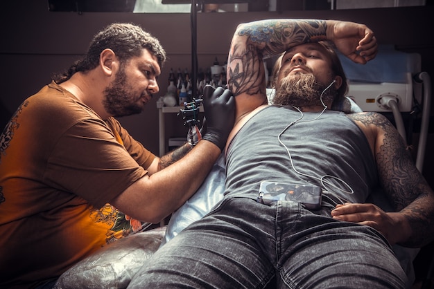 Il tatuatore professionista fa il tatuaggio in studio. / Maestro del tatuaggio che fa un tatuaggio in salone.