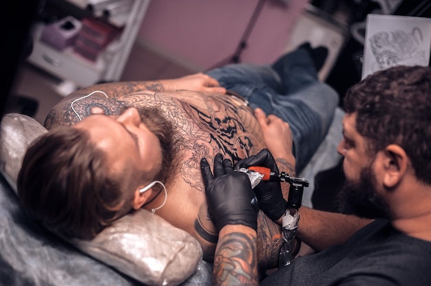 Il tatuatore professionista fa il tatuaggio sulla pelle del suo cliente