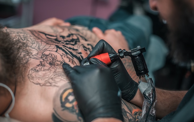 Il tatuatore professionista fa un tatuaggio sulla pelle in uno studio di officina