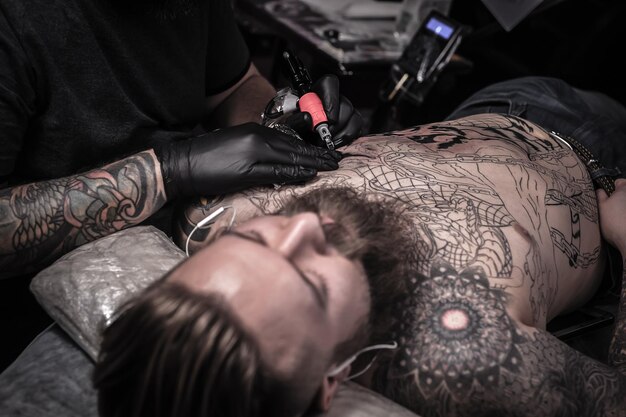 Il tatuatore tatua sulla pelle del suo cliente in uno studio di laboratorio.