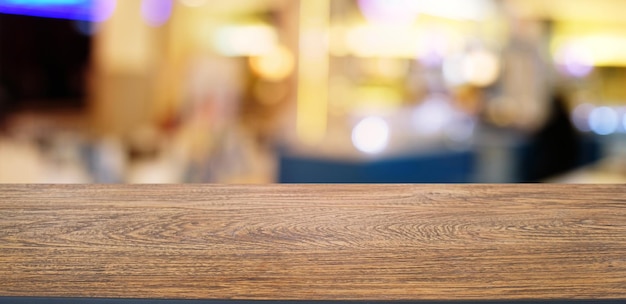 Il tavolo vuoto in legno scuro di fronte allo sfondo bokeh sfocato astratto del ristorante può essere utilizzato per visualizzare o montare i tuoi prodottiMock up per lo spazio