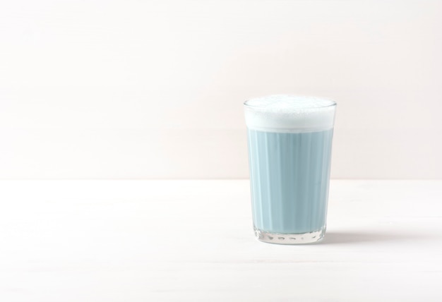 Il tè blu matcha latte con schiuma è in un bicchiere su un bianco.