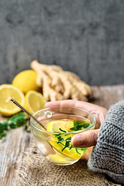 Il tè caldo con limone, zenzero e menta in una tazza di vetro è tenuto dalla mano della ragazza