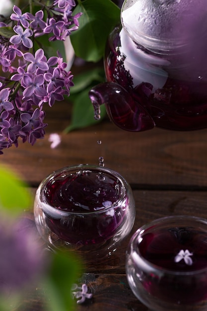 Il tè viola viene versato da una teiera di vetro nelle tazze I fiori lilla sono tutt'intorno