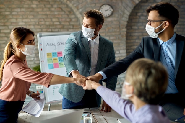 Il team aziendale felice che indossa maschere protettive mentre si scontra con i pugni durante una riunione in ufficio