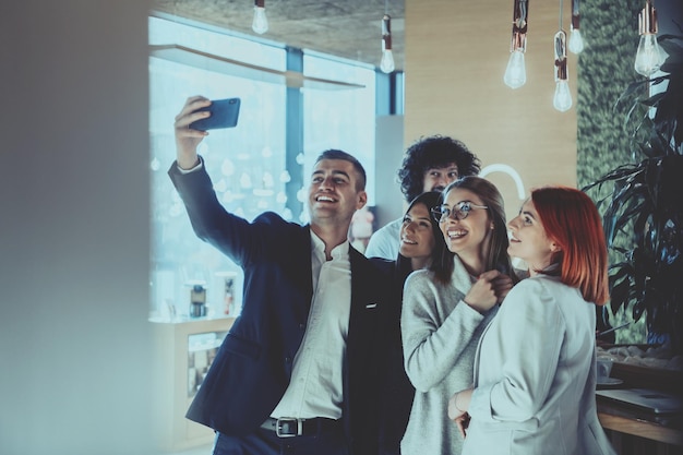 Il team del gruppo di uomini d'affari che scatta una foto selfie insieme all'ufficio open space di coworking di avvio. Messa a fuoco selettiva.