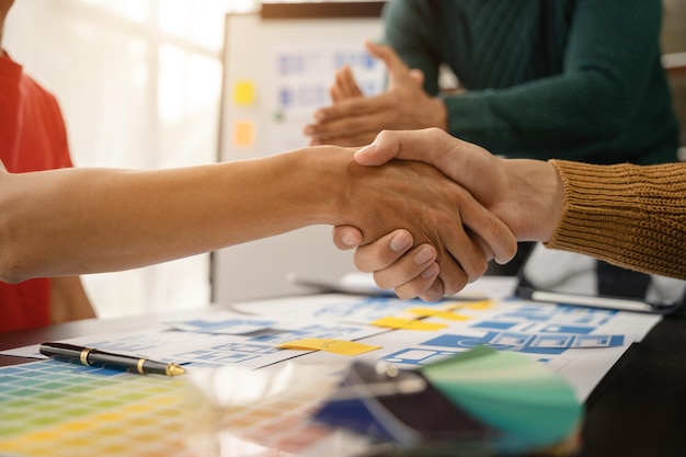 Il team di designer stringe la mano con fiducia all'investitore professionista che lavora con il nuovo progetto di avvio in una riunione d'ufficio