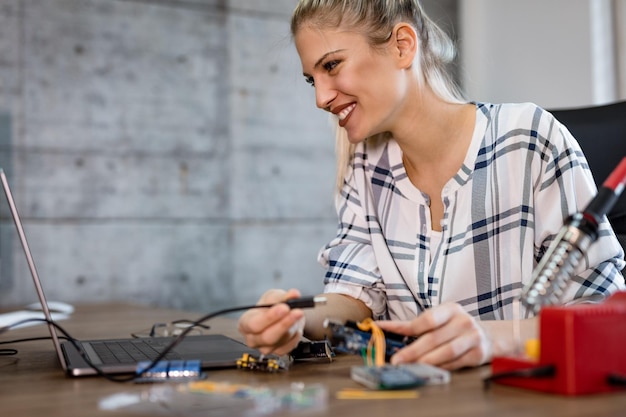 Il tecnico della giovane donna sorridente si è concentrato sulla riparazione di apparecchiature elettroniche e sul controllo di qualcosa sul laptop.