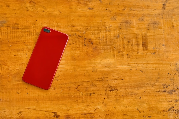 Il telefono astuto rosso si trova a faccia in giù sulla tavola di legno. Vista dall'alto