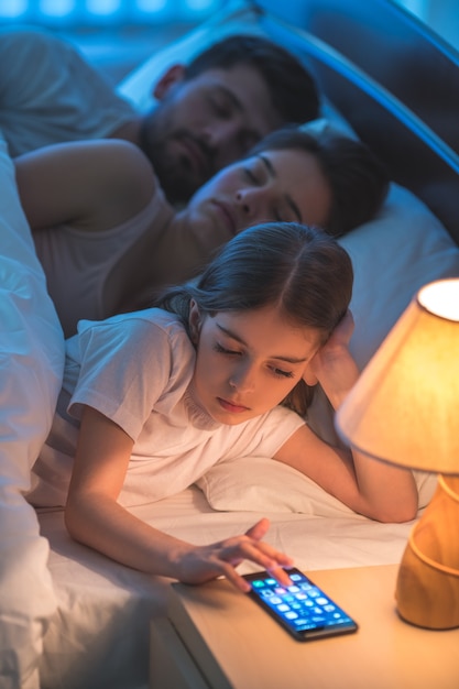 Il telefono della bambina vicino ai genitori nel letto. notte