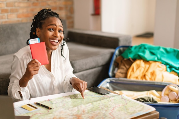 Il tempo per le vacanze ha eccitato la donna di colore che tiene il passaporto con i biglietti e indica la preparazione della mappa