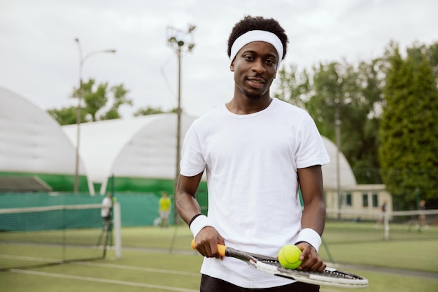 Il tennista sicuro si trova sul campo da tennis e posa per la foto che tiene in mano la racchetta da tennis