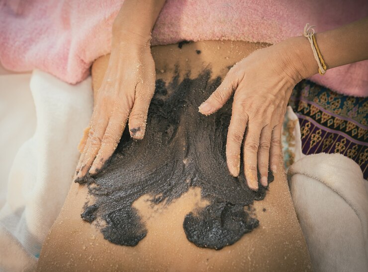 Il terapeuta sta applicando lo scrub al caffè carbone su una donna