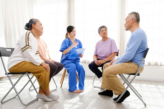 Il terapista caregiver siede con un gruppo di anziani asiatici in cerchio per controllare la salute fisica e mentale in una sessione di terapia di gruppo per anziani La casa di cura facilita un gruppo di supporto