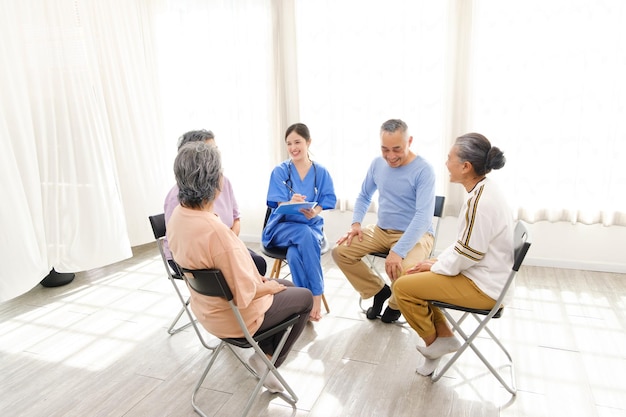 Il terapista caregiver siede con un gruppo di anziani asiatici in cerchio.