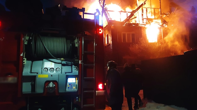 Il tetto della casa è in fiamme L'edificio residenziale brucia il villaggio I vigili del fuoco hanno spento un incendio I fari dei camion dei pompieri e il segnale della sirena del pannello