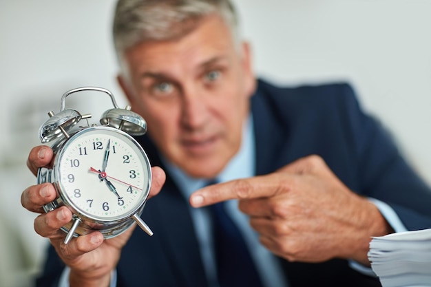 Il ticchettio degli orologi Ritratto di un uomo d'affari maturo che gesturing verso un orologio nella frustrazione