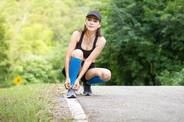 Il trasduttore auricolare asiatico di usura della donna si è inginocchiato per fare i lacci delle scarpe dopo l&#39;esecuzione dell&#39;allenamento di esercizio