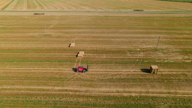Il trattore agricolo raccoglie la paglia di grano in briket per il trasporto Vista aerea Macchine agricole