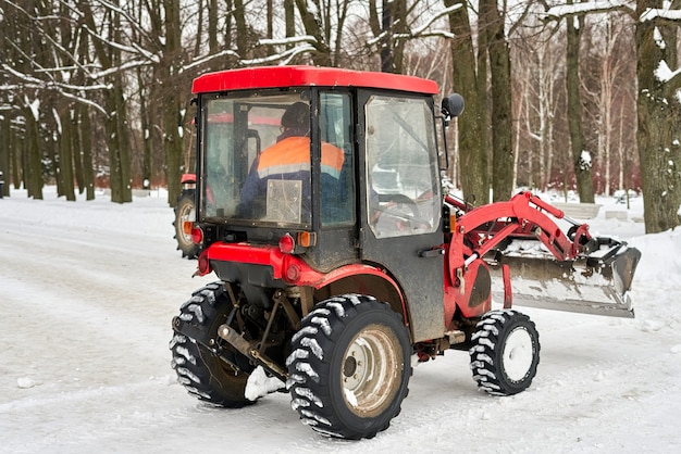 Il trattore rosso con un secchio di neve in preghiera pulisce il parco