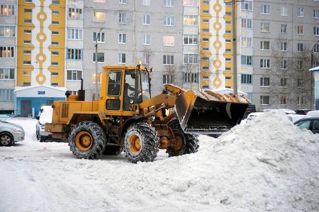 Il trattore spala la neve in un mucchio nel cortile.