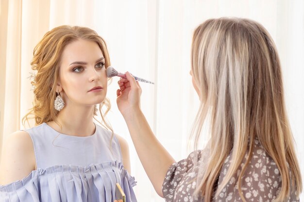 Il truccatore mette il trucco sul modello della ragazza. Pennello applica ombre, correttore. bella ragazza modello, ritratto. Colori nudi nel trucco. trucco da sposa, trucco da sera.