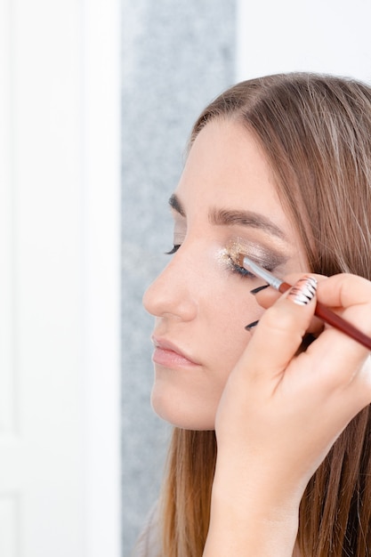 Il truccatore professionista applica il trucco a una bellissima modella. Il volto di una ragazza con la pelle pulita. Concetto di trucco e cosmetologia della vita reale. Matrimonio, sera, trucco naturale.