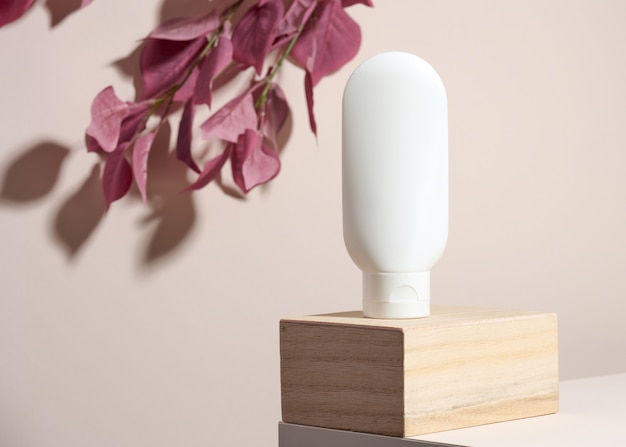 Il tubo di plastica bianco vuoto per i cosmetici si erge su un podio di legno su uno sfondo beige con ombra. Contenitori per creme, shampoo, sostanze liquide. Marchio, modello