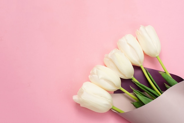 Il tulipano bianco fresco fiorisce il mazzo sulla superficie rosa pastello. copia spazio e laici piatta.