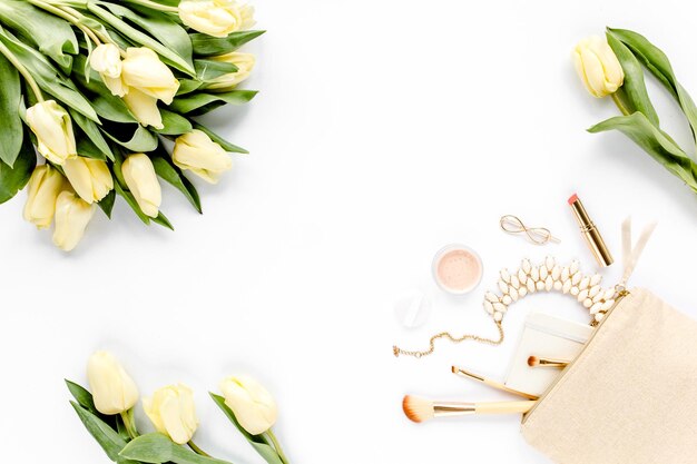 Il tulipano giallo fiorisce la borsa cosmetica beige i pennelli per il trucco i cosmetici gli accessori dorati su backgro bianco