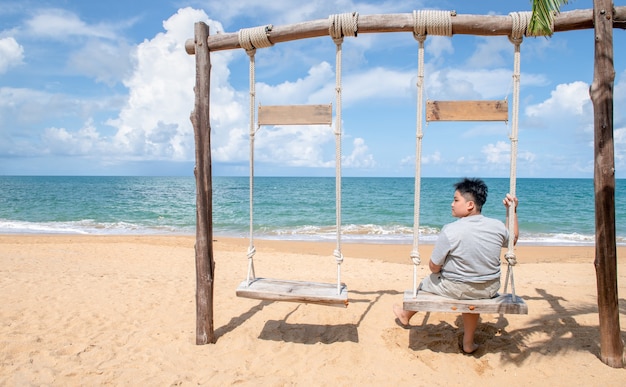 Il turista felice si siede e si rilassa sull'altalena di legno di fronte alla spiaggia, si rilassa e si riposa sul concetto di vacanza