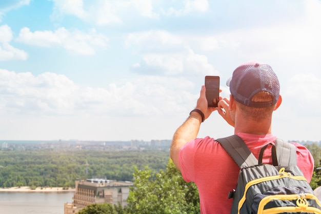 Il turista fotografa al telefono una bellissima vista della città. L'uomo è in piedi con le spalle