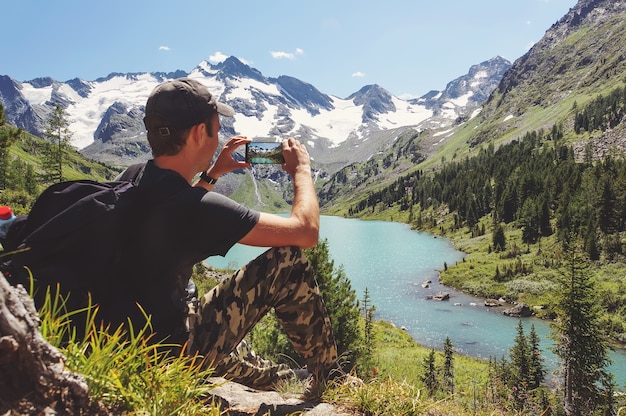 Il turista in maglietta nera scatta foto con lo smartphone sul picco della roccia. Paesaggio collinare da sogno sottostante. Il bellissimo paesaggio dei Monti Altai. Lago Multinskoe