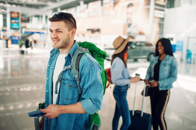 Il turista maschio con lo zaino tiene il passaporto in aeroporto. Passeggeri con bagaglio in aerostazione, viaggio felice, viaggio estivo