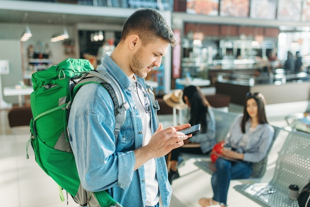 Il turista maschio con lo zaino tiene il telefono cellulare, i viaggiatori di sesso femminile in attesa della partenza in aeroporto.