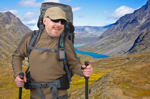 Il turista maschio felice con lo zaino sta viaggiando negli altopiani