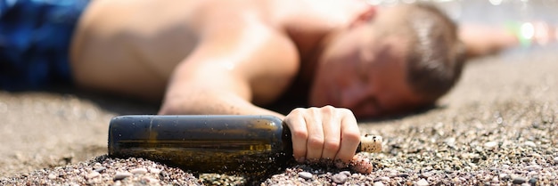 Il turista maschio ubriaco si trova sulla spiaggia con una bottiglia di vino che beve alcolici sul concetto di vacanza