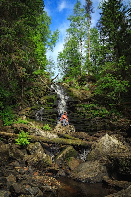 Il turista si siede su una roccia vicino ad una cascata della foresta.