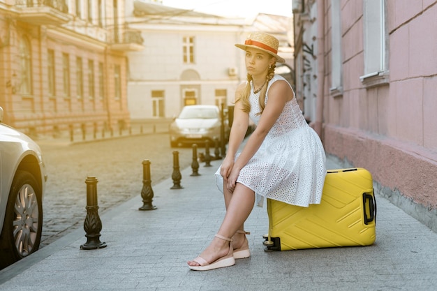 Il turista stanco della giovane donna si siede su una grande valigia gialla. Il concetto di uno stile di vita attivo e turistico.