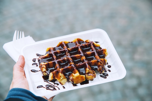 Il turista tiene in mano il popolare cibo di strada Belgio gustoso waffle con salsa al cioccolato