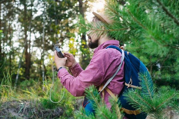 Il turista tiene in mano uno smartphone con un caricabatterie portatile. L'uomo con un Power Bank carica il telefono sullo sfondo della natura e della foresta.