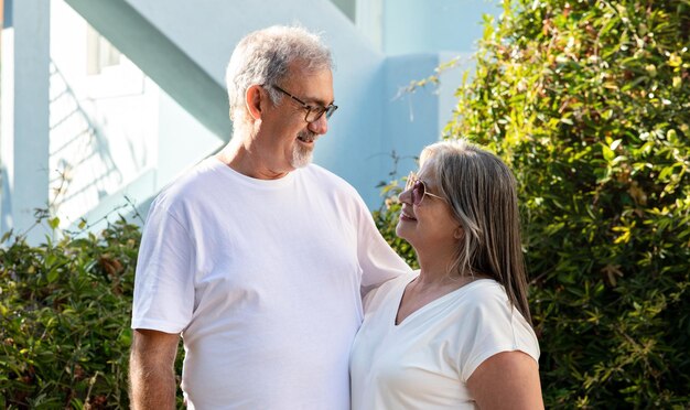 Il vecchio marito e la moglie europei sorridenti in magliette bianche che si abbracciano si godono il tempo libero all'aperto