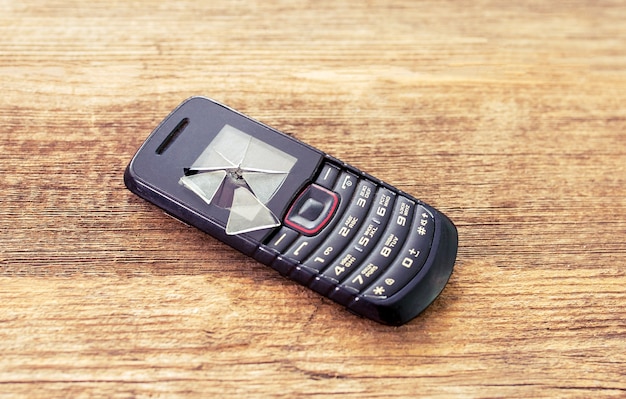Il vecchio telefono nero con i pulsanti giace su uno sfondo di legno con uno schermo danneggiato