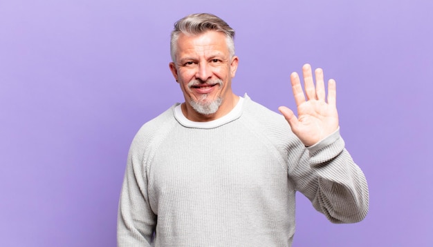 Il vecchio uomo anziano sorride allegramente e allegramente, agita la mano, ti dà il benvenuto e ti saluta, o ti saluta