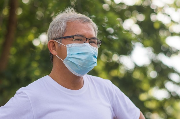 Il vecchio uomo asiatico cammina all'aperto e indossa una maschera medica