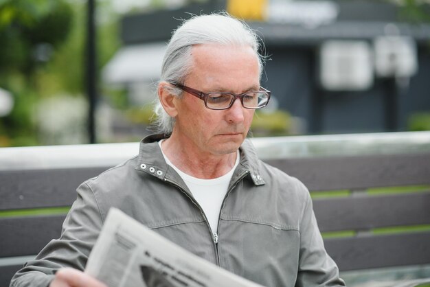 Il vecchio uomo dai capelli grigi riposa sulla panchina nel parco estivo