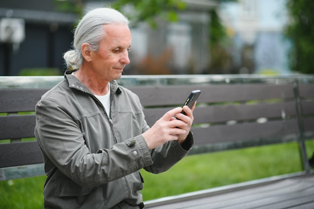 Il vecchio uomo dai capelli grigi riposa sulla panchina nel parco estivo