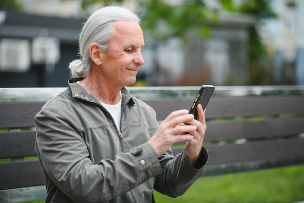 Il vecchio uomo dai capelli grigi riposa sulla panchina nel parco estivo