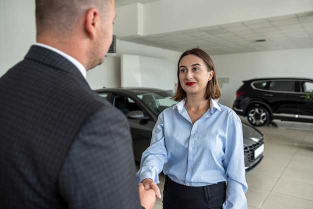 Il venditore di auto sorridente stringe la mano a una brunetta che vuole comprare un'auto